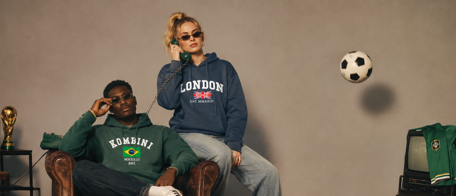 Two people sitting on a couch wearing hoodies with text, a soccer ball in the air, and sports equipment on a shelf.